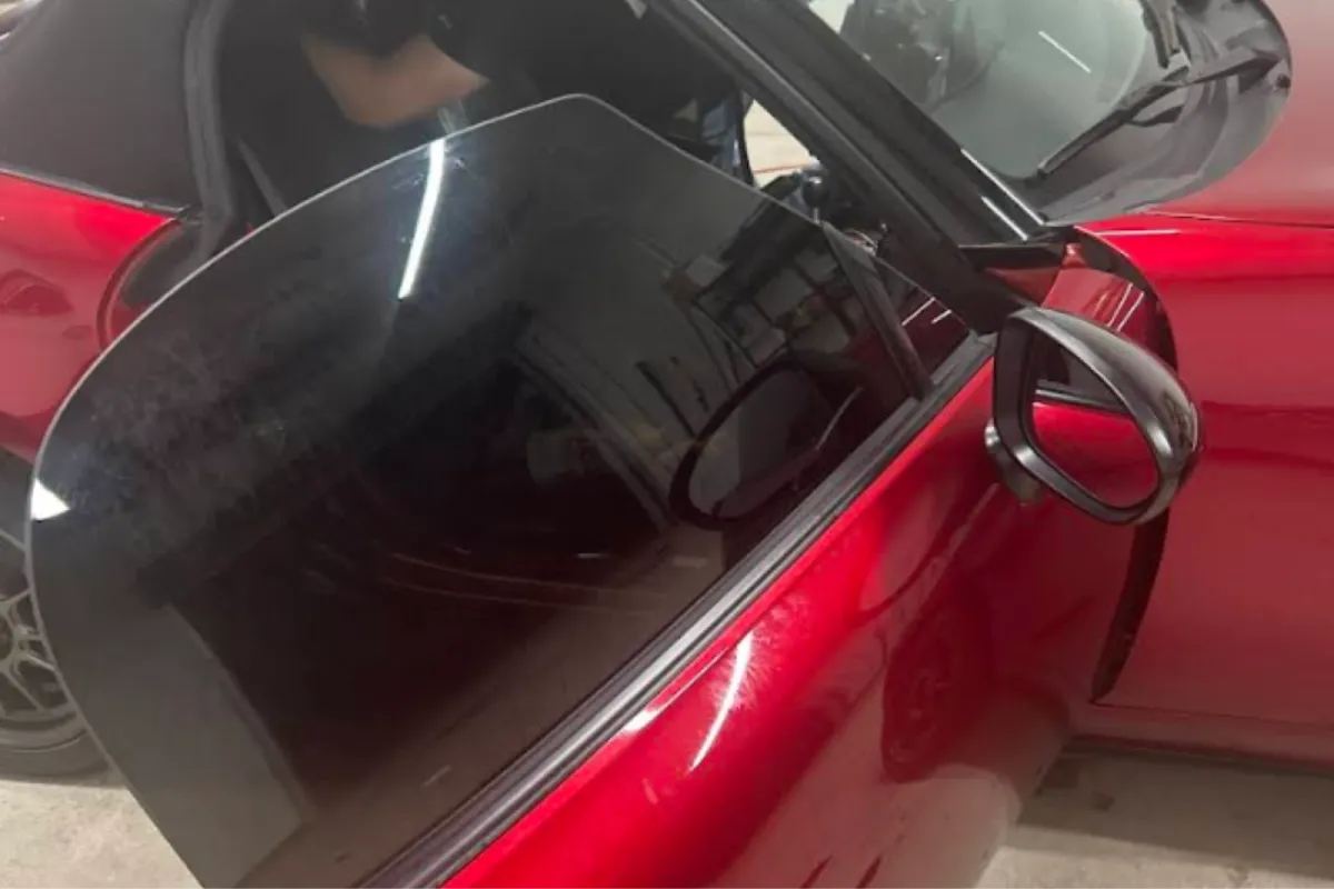 A close-up of a red car with the window tinting film applied, showing the contrast between the tinted and non-tinted areas of the window.