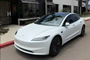A white Tesla sedan parked outside a building, with a clean and modern design.