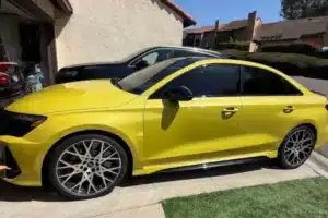 A yellow Mercedes sedan with dark-tinted windows parked in front of a residential building.