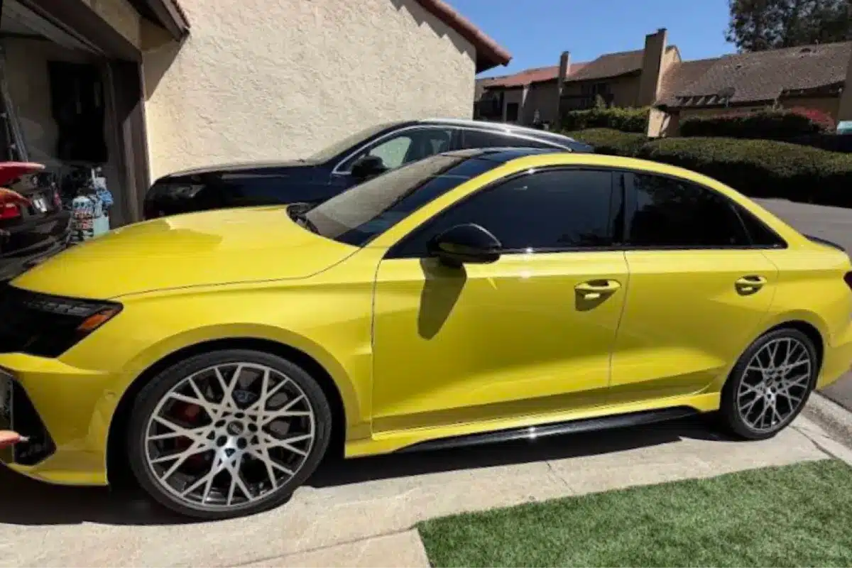 A yellow Mercedes sedan with dark-tinted windows parked in front of a residential building.
