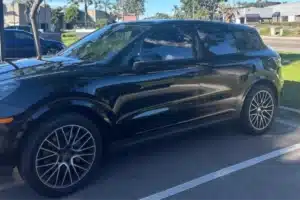 Black Porsche SUV with dark window tint in parking lot.