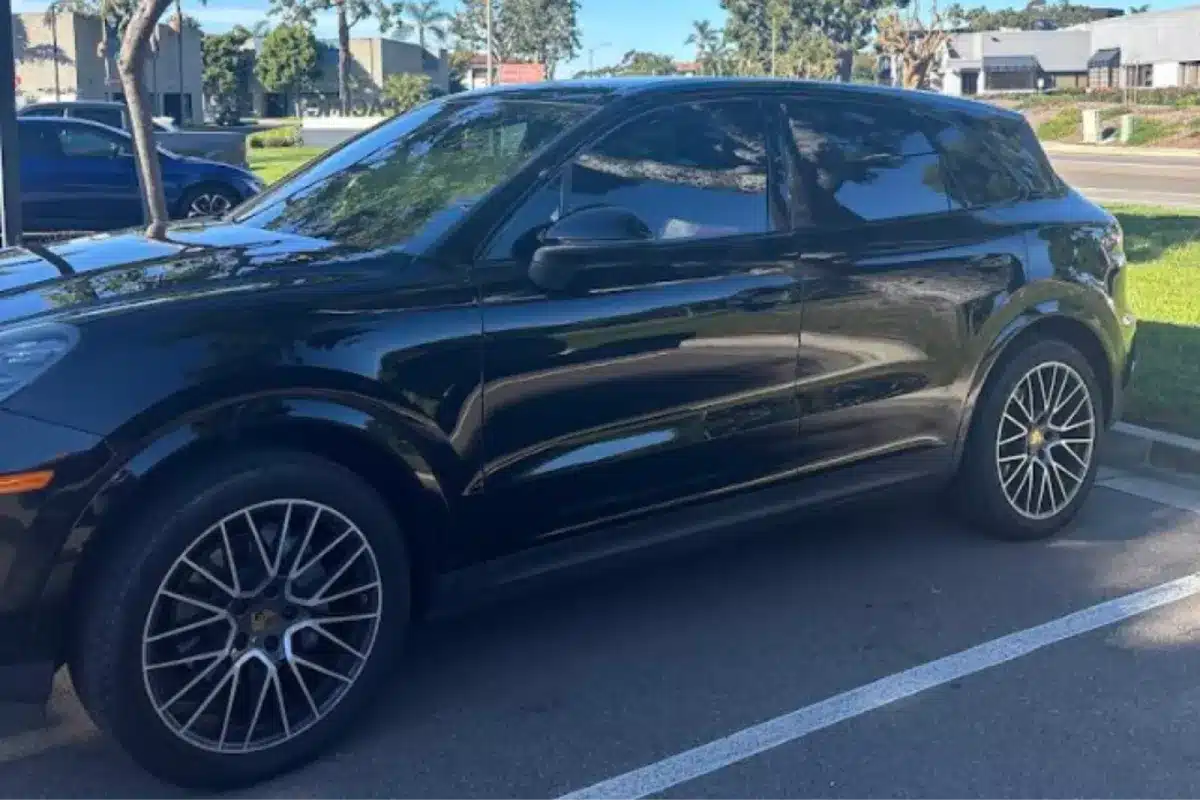 Black Porsche SUV with dark window tint in parking lot.